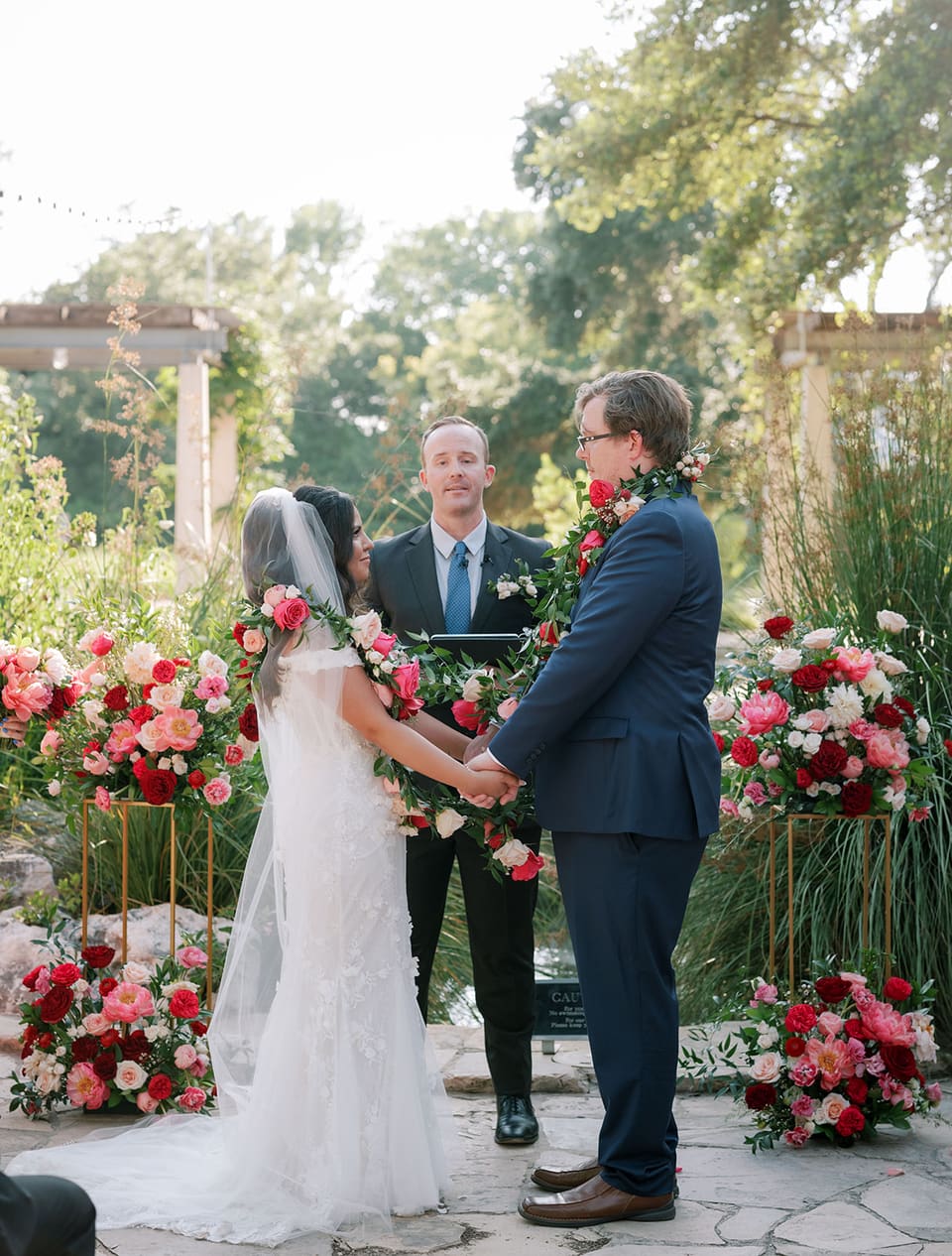 Bride and groom holding hands wrapped in a floral garland during their ceremony at LBJ Wildflower Center